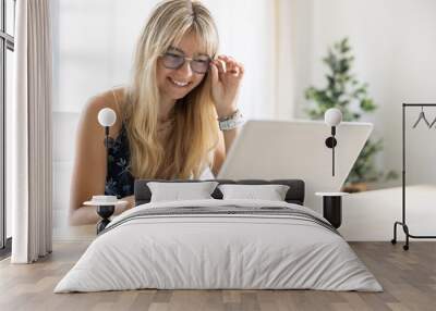 Portrait of happy young beautiful woman sitting with laptop, using glasses Wall mural