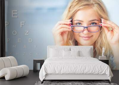 Portrait of young woman holding glasses and looking at camera. Ophthalmological concept with eye test chart Wall mural