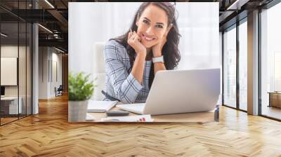 Pretty businesswoman smiles at the camera while sitting at her desk in front of the computer Wall mural