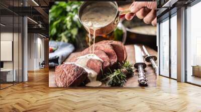 Rump steak cut to slices on a chopping board next to a knife and rosemary, with a mushroom sauce poured over it Wall mural