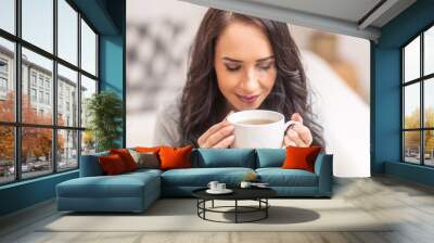 Young brunette woman holding a cup of tea or coffee and smelling lovely aroma Wall mural