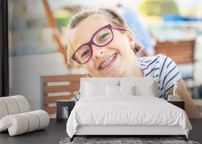 Young preteen girl in glasses wearing braces smiles at the camera on a summer day Wall mural