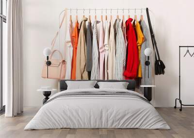 Fashionable clothes on hangers on a wardrobe rack on a light background. Wall mural