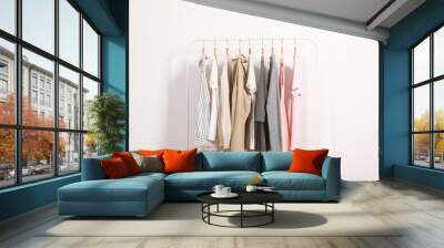 Fashionable clothes on hangers on a wardrobe rack on a light background. Wall mural