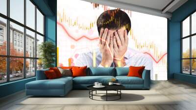 A man holds his face in frustration in front of a stock market graph showing declining trends on a white background, signifying financial distress Wall mural