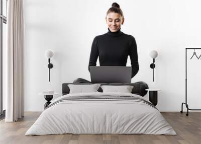 A smiling young woman sitting cross-legged with a laptop on a white background, embodying a casual business concept Wall mural