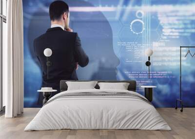 Attractive young european businessman standing in blurry office interior with abstract glowing tech head outline hologram. Machine learning and ai concept. Double exposure. Wall mural