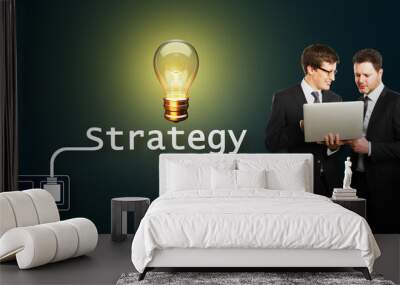 Businessmen discussing strategy with glowing lightbulb symbolizing idea on dark background. Wall mural