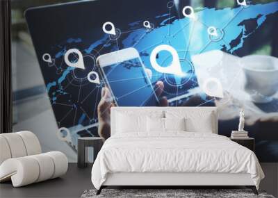 Geolocation and distributed data concept with hologram world map model and white pinpoints on man hands using cell phone and laptop backdrop Wall mural