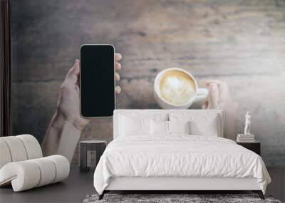 Man hand with blank smartphone and cup of coffee on wooden table Wall mural