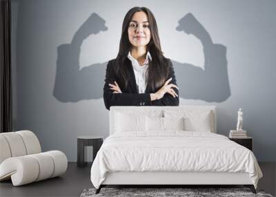 Portrait of attractive young european businesswoman with folded arms and shadow muscle arms on concrete wall background. Strenght and leadership concept. Wall mural