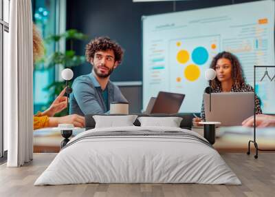 Team collaborating in a modern office, discussing ideas around a table with laptops and charts on a bright background. Wall mural