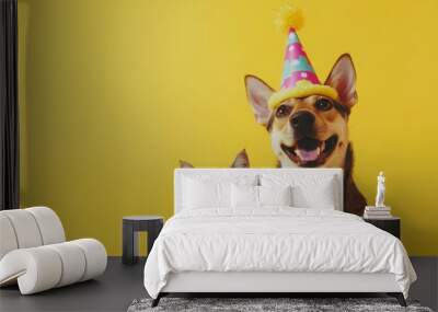 An adorable dog wearing a colorful party hat, playfully sitting next to a curious cat, all set against a bright yellow background Wall mural