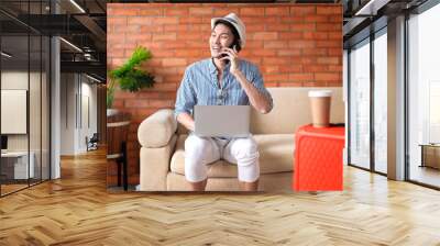 Asian male man digital nomad hand working with notebook laptop while waiting talking conversation business discussion at lobby,ready to travel asia tourist smiling cheerful sit on sofa hotel lobby Wall mural