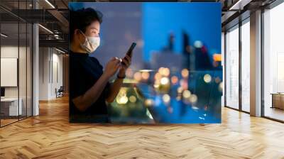 attractive asian female woman wear protecting mask hand use smartphone technology communication with background of bokeh light urban building background business ideas concept Wall mural