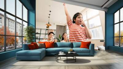 happiness pleasure asian lovely family enjoy watch and cheer up little daughter girl singing and dance practice in front of tv in living room Wall mural