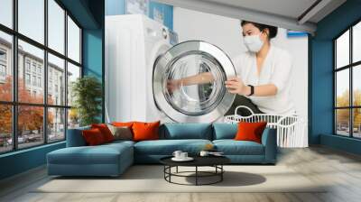 portrait asian female wear virus protecting mask in spread of covid-19 washing  in blue color interior laundry shop in condoiminuim city  new normal lifestyle Wall mural