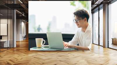 Smart attractive positive asian business male wearing glasses work remote new normal lifestyle hand use laptop tele conference onlive videocall meeting remote business ideas concept Wall mural