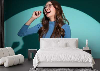 Smiling optimistic Asian casual female woman in blue sweater wear glasses hand playing fun gesture holding her body shape positive thinking portrait shot studio shooting on blue colour background Wall mural