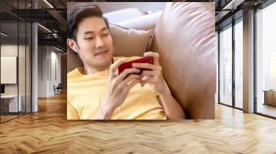 young asian male hand playing smartphone gaming online casual and leisure exiting and jpyful laydown on sofa on weekend at home quarantine activity ideas concept Wall mural