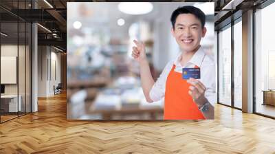 young smart attractive asian male reatuarant owner hand sign ok with credit card online purchase order online from home concept asian apron uniform smile warm welcome for appllication order Wall mural