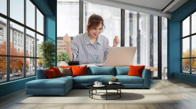 Beautiful Asian businesswoman celebrate while using laptop at office and showing delight. Startup small business and successful concept Wall mural