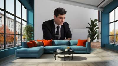 Perplexed, puzzled handsome businessman looking at laptop screen at workplace in office. Young CEO or project manager is not sure whether he should agree to the deal, sign contract, buy stock shares. Wall mural