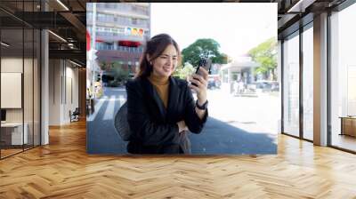 Smiling Asian businesswoman wearing a suit stands tall in the city using an application on her mobile phone. Read news on your smartphone fast connection Check outdoor mobile apps Wall mural