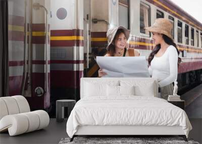 Two women look at tourist maps while waiting to travel at the train station. Wall mural