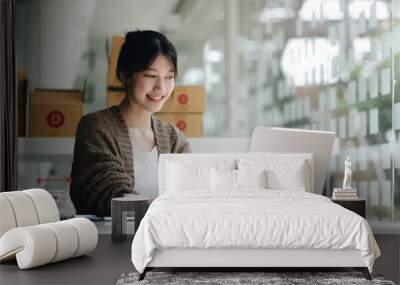 Young attractive asian woman owner startup business look at camera work happy with box at home prepare parcel delivery in sme supply chain, procurement, omnichannel or coronavirus quarantine concept. Wall mural