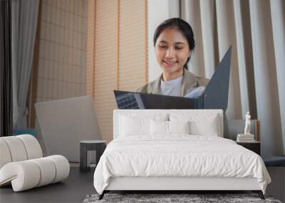 Young Business Woman Sitting at Desk Reviewing Documents with Laptop in Modern Office Setting Wall mural