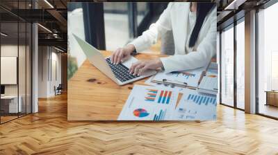 Businesswoman Analyzing Data:  A focused businesswoman works diligently on her laptop, surrounded by financial charts and reports, showcasing professionalism and dedication.  Wall mural