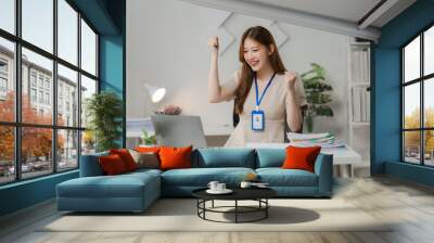 Success Story: A young businesswoman celebrates a significant achievement, her hands raised in triumph as she stares triumphantly at her laptop screen, radiating joy and determination. The image conve Wall mural