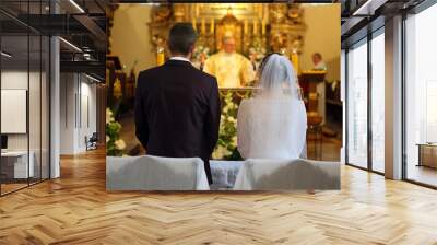 A young couple stands in front of the altar during a wedding ceremony in a Catholic church. Wall mural