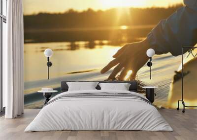 man puts fingers down in lake kayaking against backdrop of golden sunset, unity harmony nature Wall mural