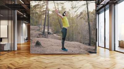 Young runner in sports clothes warms up before cardio training in pine forest. Man in headphones stretches muscles before jogging slow motion Wall mural