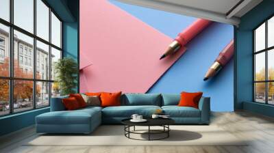 Minimalist setup with pink paper sheets and two pink pencils on a blue background. The soft color palette conveys creativity and elegance in a refined workspace. Wall mural