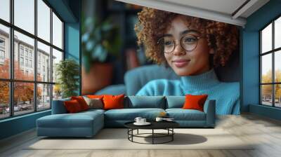 Young woman with curly hair and glasses in a cozy setting, thoughtful expression, relaxed and comfortable atmosphere in soft lighting Wall mural