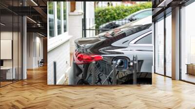 Electric car on charge plugged in at home outside residential buildings Wall mural