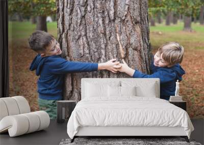 Two little brothers boys hugging a tree in the wood and smiling Wall mural