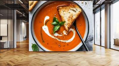 A bowl of creamy tomato soup with a swirl of cream and basil leaves, accompanied by a slice of toasted bread Wall mural