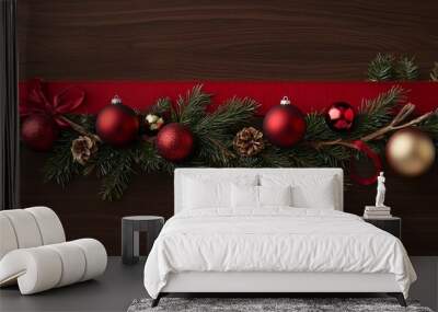 Classic holiday decoration style with a bright red ribbon, evergreen sprigs, and shiny red and gold ornaments on a deep, rich wooden background. Wall mural