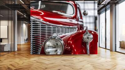 Detailed close-up of a red vintage automobile's grille and headlights in a gray garage, capturing the essence of automotive history and design Wall mural