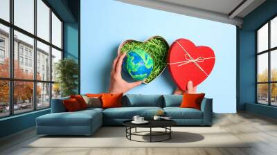 Female hands holding heart gift box with planet earth on a blue background. Earth Day. Wall mural