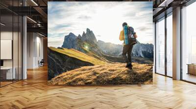 Young man hiking at Seceda mountain peak at sunrise. Backpack, yellow jacket, boots, beanie. Traveling to puez Odle, Dolomites, Trentino, Italy. Wall mural