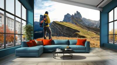 Young man hiking at Seceda mountain peak at sunrise. Backpack, yellow jacket, boots, beanie. Traveling to puez Odle, Dolomites, Trentino, Italy. Wall mural