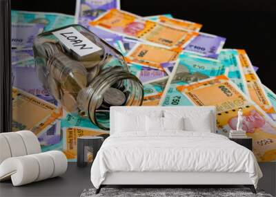 High angle shot of an opened glass jar with coins and money notes scattered on black background. Wall mural