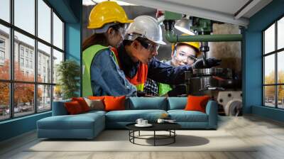 Asian foreman manager showing case study of factory machine to two engineer trainee young woman in protective uniform. teamwork people training and working in industrial manufacturing business Wall mural