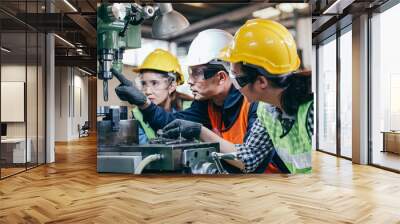 Asian male foreman manager showing case study of factory machine to two engineer trainee young woman in protective uniform. teamwork people training and working in industrial manufacturing business Wall mural