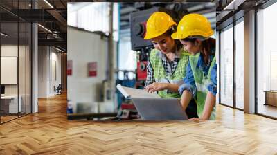 Two female engineers or technician worker wearing safety hard helmet discuss project in industry manufacturing factory. woman using laptop checking work, team colleague note on checklist document Wall mural